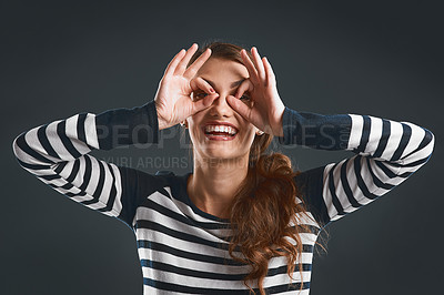 Buy stock photo Studio portrait of a cheerful young woman making a face with her hands while standing against a dark background