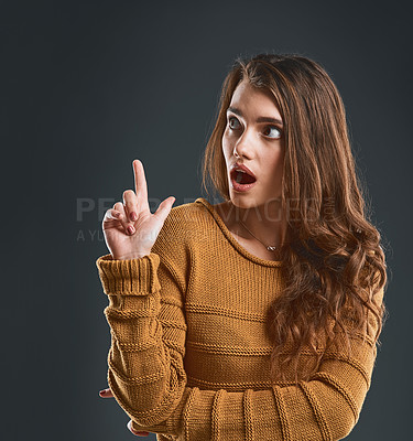 Buy stock photo Studio shot of a surprised looking young woman holding up her hand while standing against a dark background
