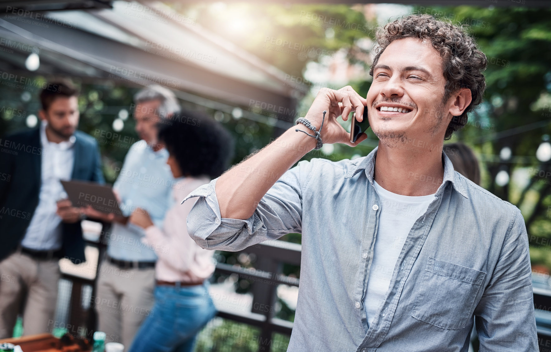 Buy stock photo Shot of a businessman talking on a cellphone outside with his colleagues in the background