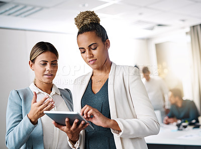Buy stock photo Shot of two businesswomen working on a digital tablet in an office