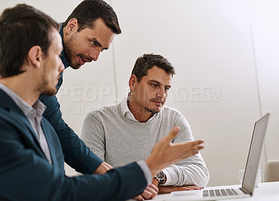 Buy stock photo Shot of a group of businessmen working together on a laptop in an office