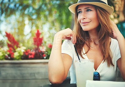 Buy stock photo Shot of a cheerful young woman wearing a hat and enjoying a cold beverage while being seated at a restaurant outside during the day