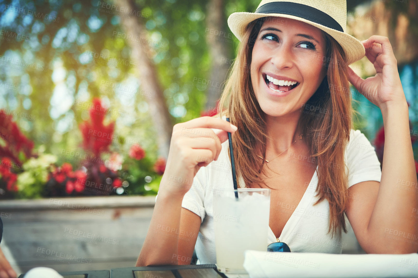 Buy stock photo Shot of a cheerful young woman wearing a hat and enjoying a cold beverage while being seated at a restaurant outside during the day