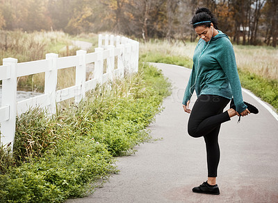 Buy stock photo Shot of an attractive young woman stretching while out for a run in nature