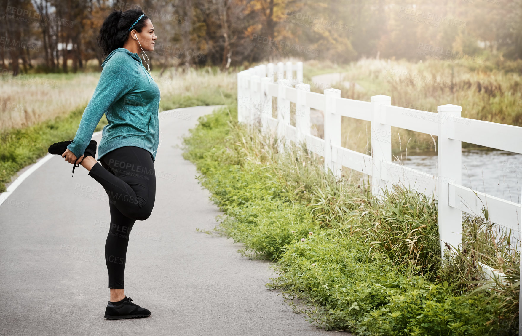 Buy stock photo Shot of an attractive young woman stretching while out for a run in nature