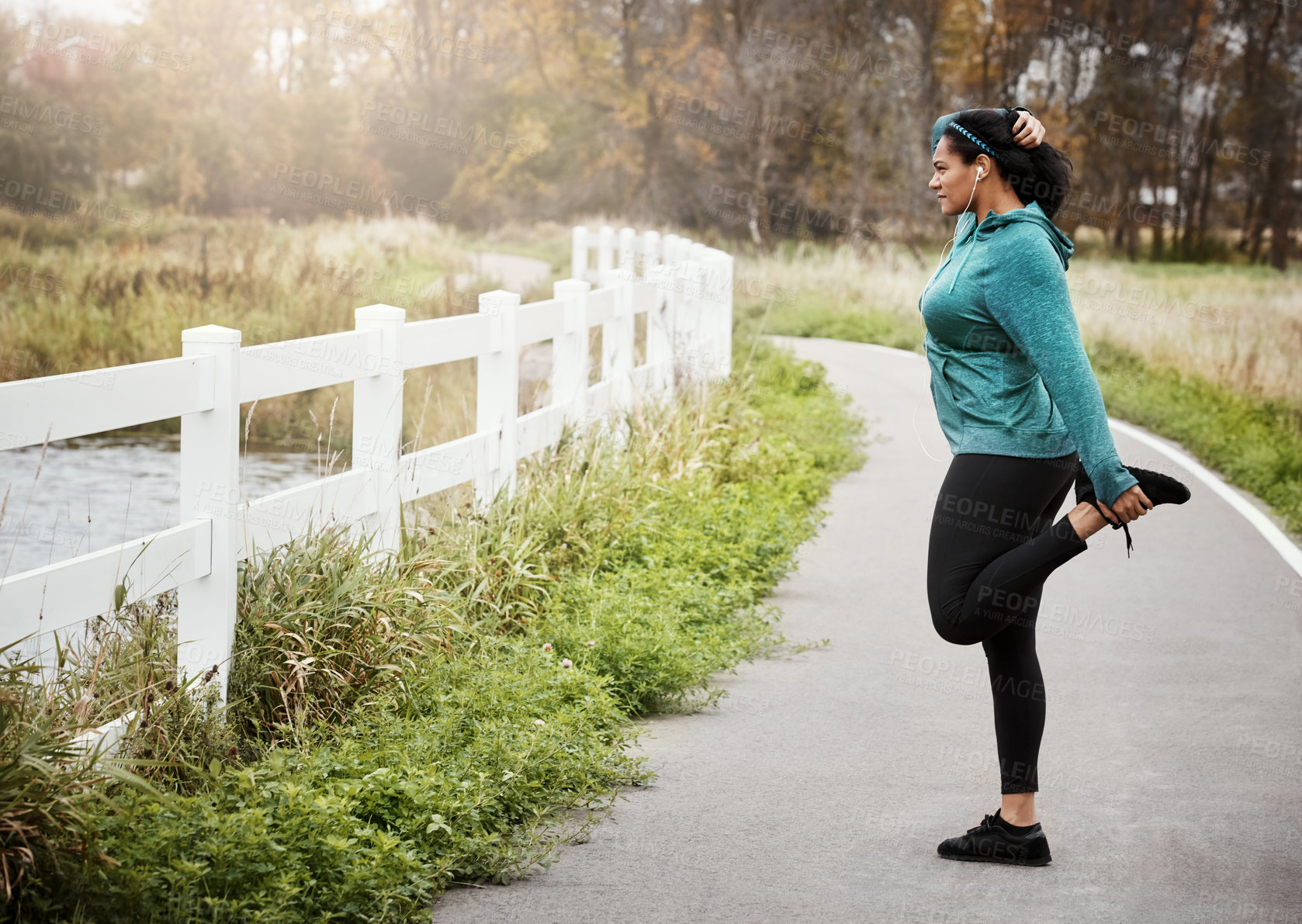 Buy stock photo Shot of an attractive young woman stretching while out for a run in nature