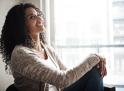 Buy stock photo Shot of a cheerful young woman relaxing while being seated on a chair at home during the day