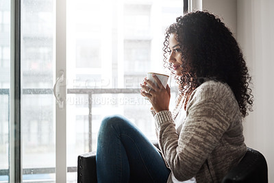 Buy stock photo Shot of a cheerful young woman enjoying a cup of coffee while being seated on a chair at home during the day