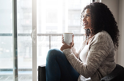 Buy stock photo Shot of a cheerful young woman enjoying a cup of coffee while being seated on a chair at home during the day