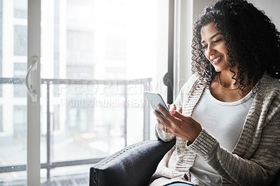 Buy stock photo Shot of a cheerful young woman relaxing while texting on her cellphone at home during the day