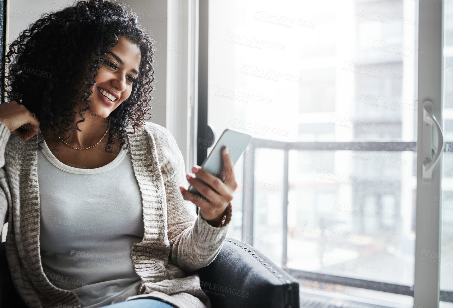 Buy stock photo Shot of a cheerful young woman relaxing while texting on her cellphone at home during the day