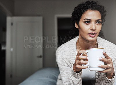 Buy stock photo Shot of a cheerful young woman drinking coffee while being seated on a couch inside at home during the day