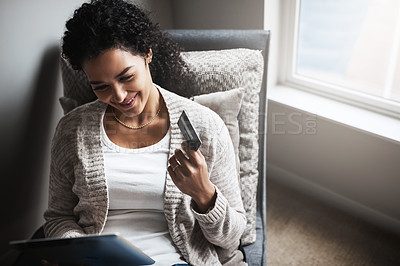 Buy stock photo Shot of a cheerful young woman relaxing on a chair while  doing online shopping on a digital tablet at home