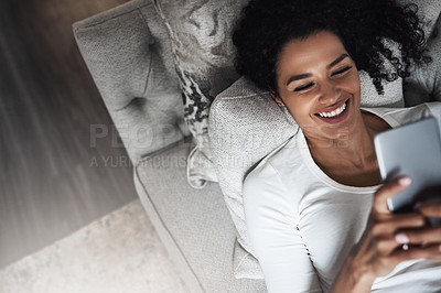 Buy stock photo Shot of a cheerful young woman relaxing on a couch while texting on her cellphone at home during the day