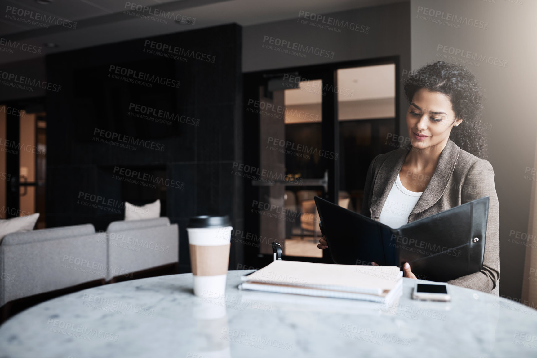 Buy stock photo Shot of a young businesswoman reading through a business folder in a cafe