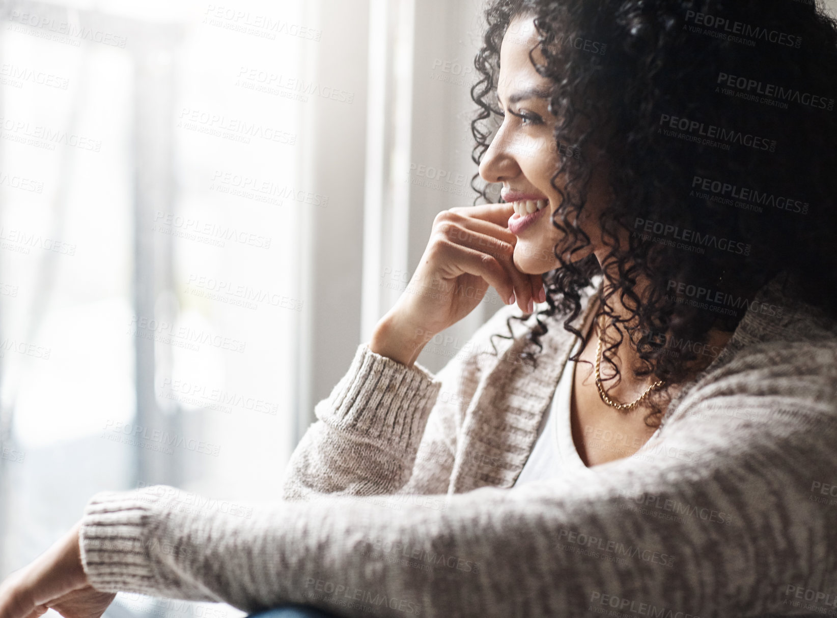 Buy stock photo Shot of a cheerful young woman relaxing while being seated on a chair at home during the day