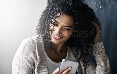 Buy stock photo Shot of a cheerful young woman relaxing while texting on her cellphone at home during the day