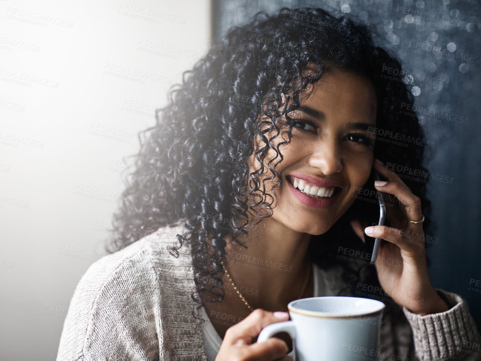 Buy stock photo Shot of a cheerful young woman relaxing and drinking coffee while talking on her cellphone at home during the day