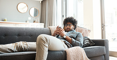 Buy stock photo Shot of a handsome young man using his cellphone while relaxing on the couch at home