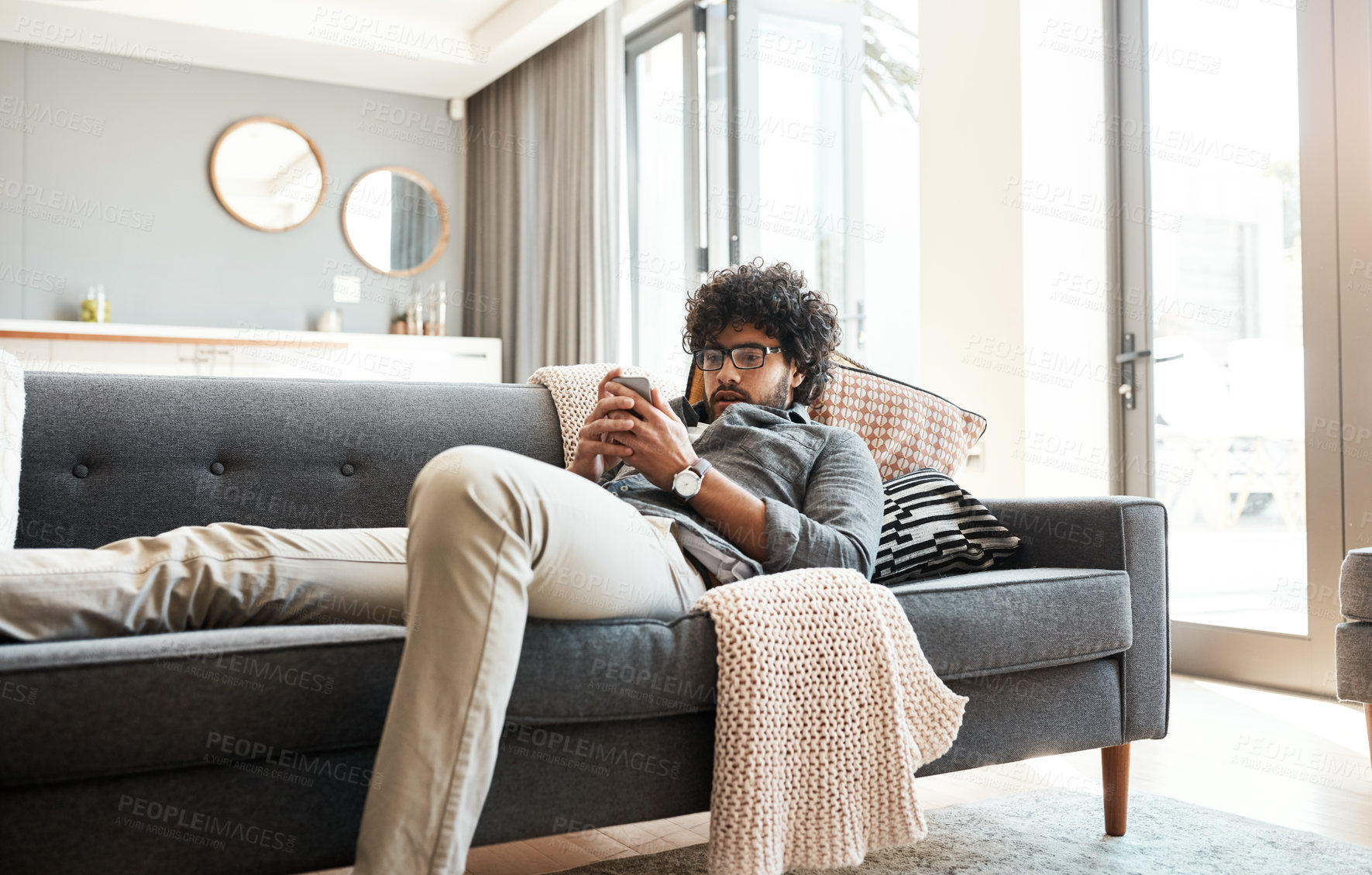 Buy stock photo Shot of a handsome young man using his cellphone while relaxing on the couch at home