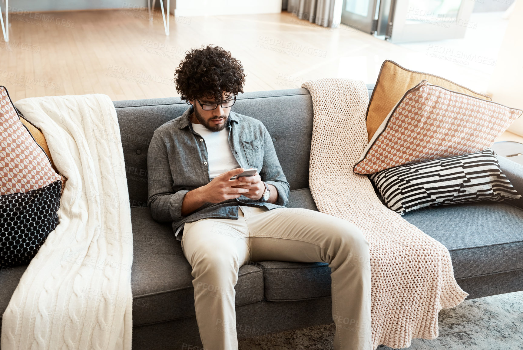 Buy stock photo Shot of a handsome young man using his cellphone while relaxing on the couch at home