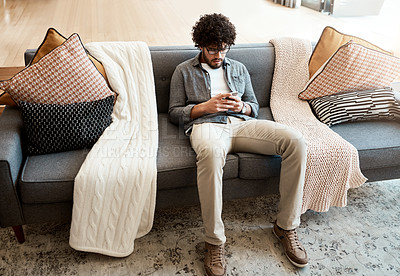 Buy stock photo Shot of a handsome young man using his cellphone while relaxing on the couch at home