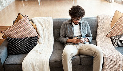 Buy stock photo Shot of a handsome young man using his cellphone while relaxing on the couch at home