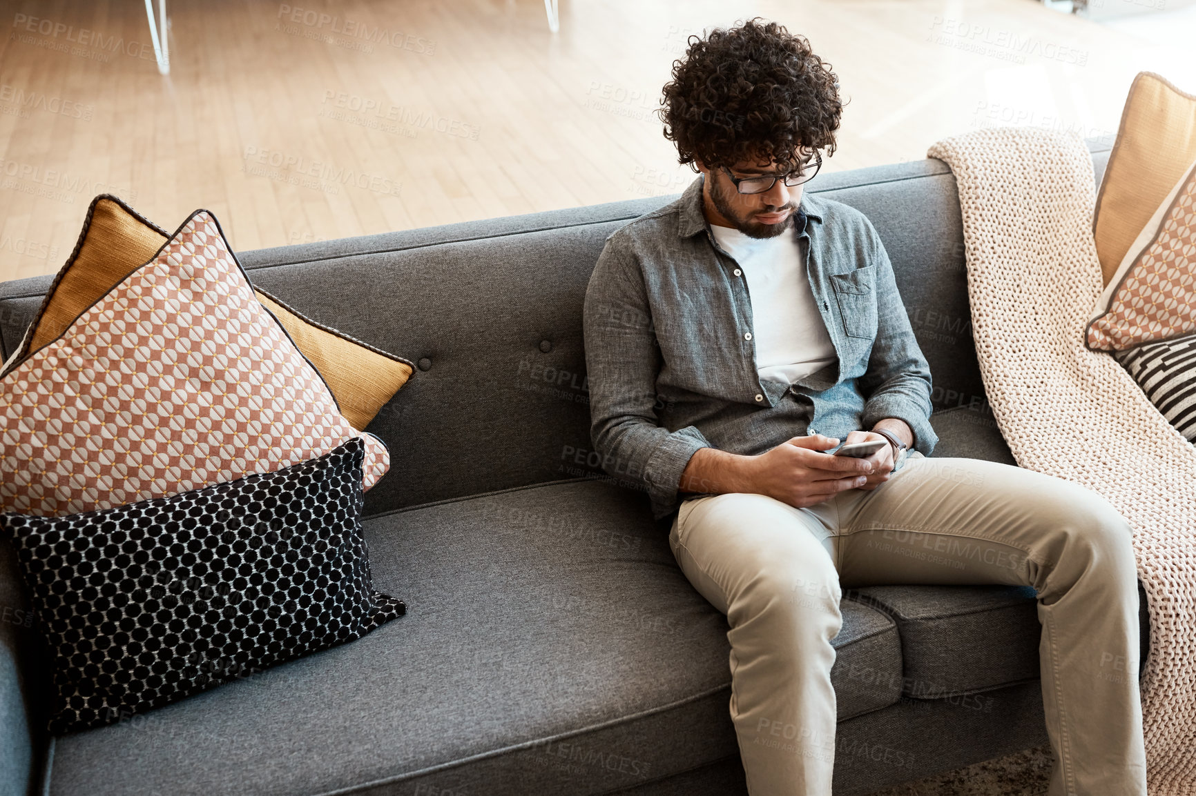 Buy stock photo Shot of a handsome young man using his cellphone while relaxing on the couch at home