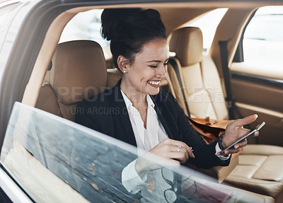 Buy stock photo Shot of a cheerful young businesswoman seated in a car as a passenger while texting on her phone on her way to work