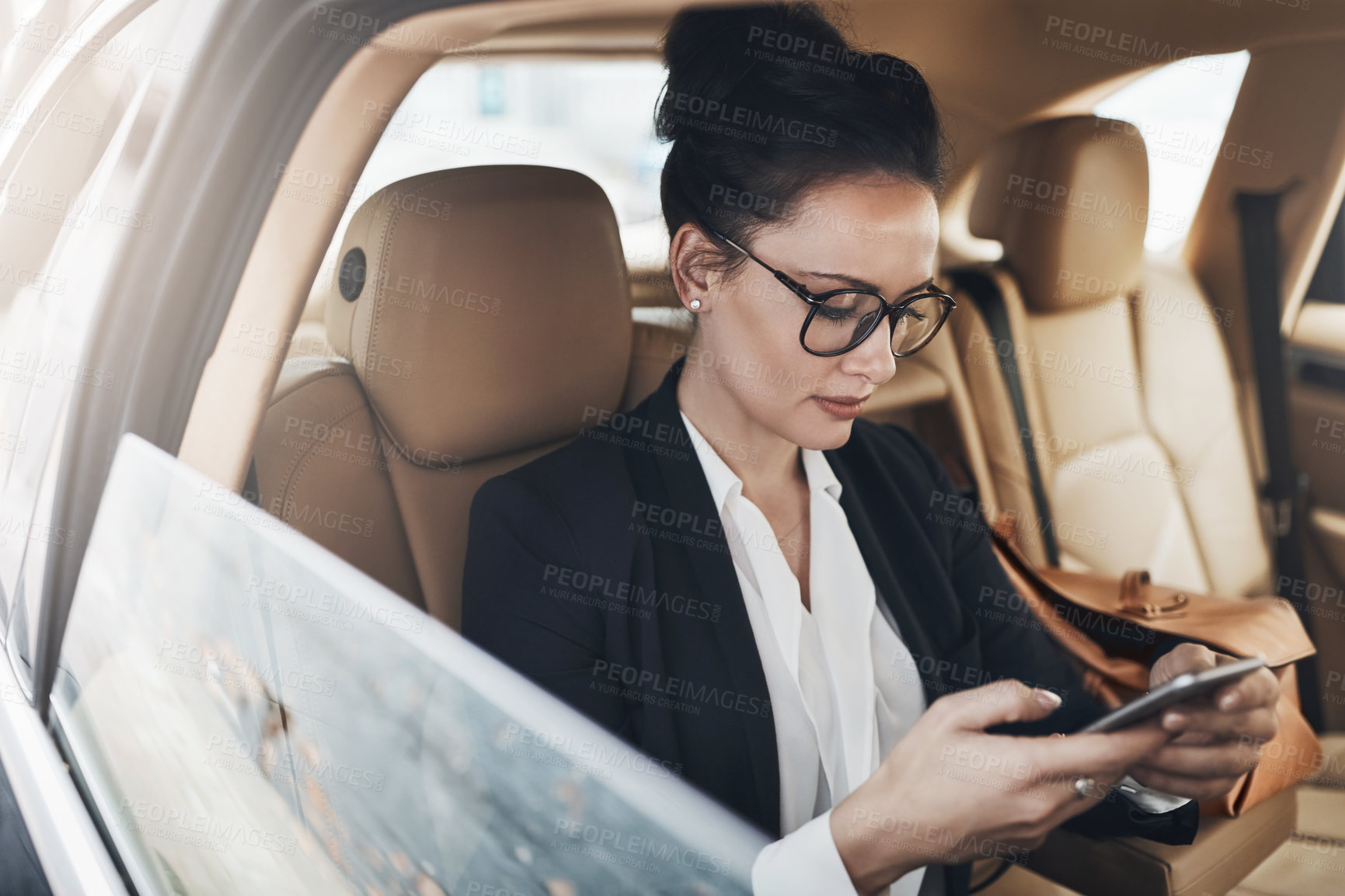 Buy stock photo Shot of a confident young businesswoman seated in a car as a passenger while texting on her phone on her way to work