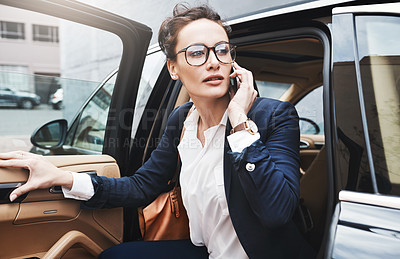 Buy stock photo Shot of a confident young businesswoman getting out of a car while holding a cellphone outside during the day