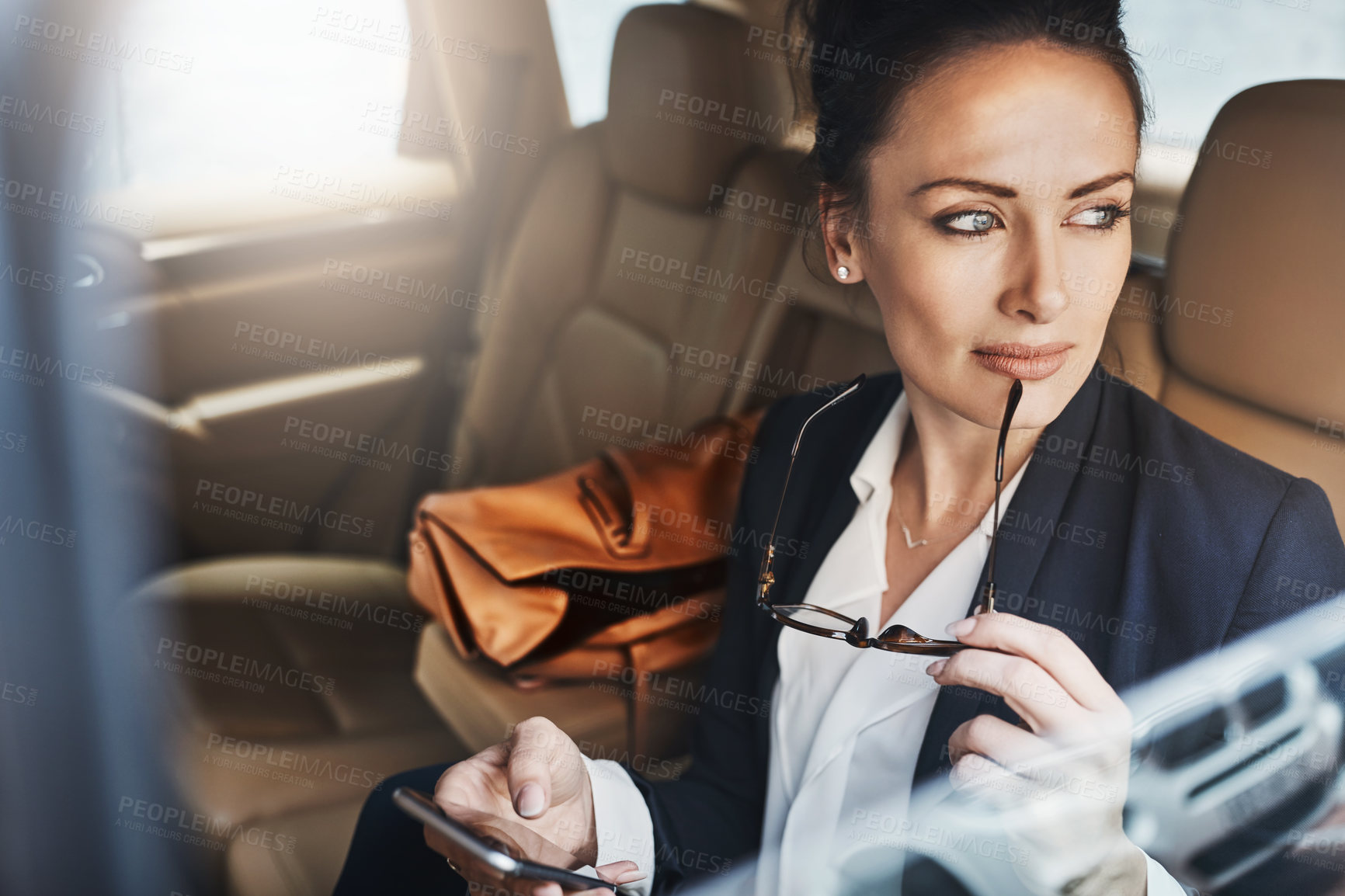 Buy stock photo Shot of a confident young businesswoman seated in a car as a passenger while busy on her phone and looking out of the window