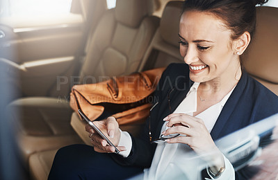 Buy stock photo Shot of a confident young businesswoman seated in a car as a passenger while texting on her phone on her way to work