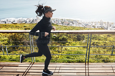 Buy stock photo Shot of a determined young woman going for a jog by herself with the mountain, city and ocean in the background