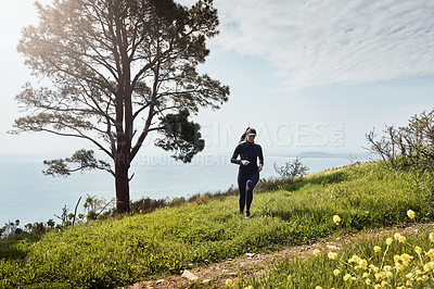 Buy stock photo Shot of a determined young woman running up a hill by herself with a nice view of the ocean in the background