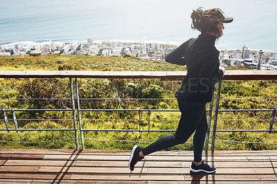 Buy stock photo Shot of a determined young woman going for a jog by herself with the mountain, city and ocean in the background