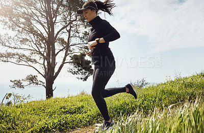 Buy stock photo Shot of a determined young woman running down a hill by herself with a nice view of the ocean in the background