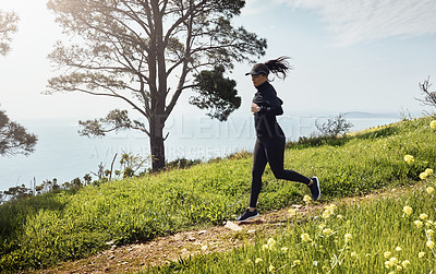 Buy stock photo Shot of a determined young woman running down a hill by herself with a nice view of the ocean in the background