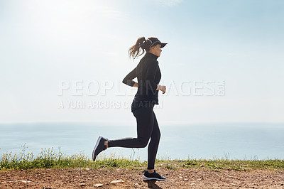 Buy stock photo Shot of a determined young woman going for a jog on her own with a view of the ocean in the background