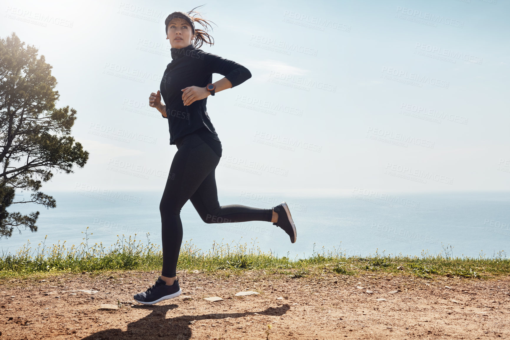 Buy stock photo Shot of a determined young woman going for a jog on her own with a view of the ocean in the background