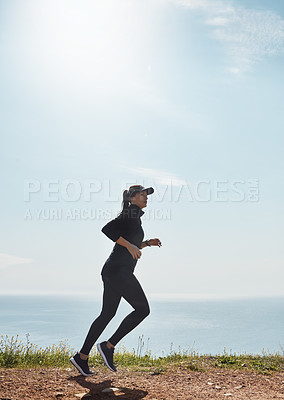 Buy stock photo Shot of a determined young woman going for a jog on her own with a view of the ocean in the background