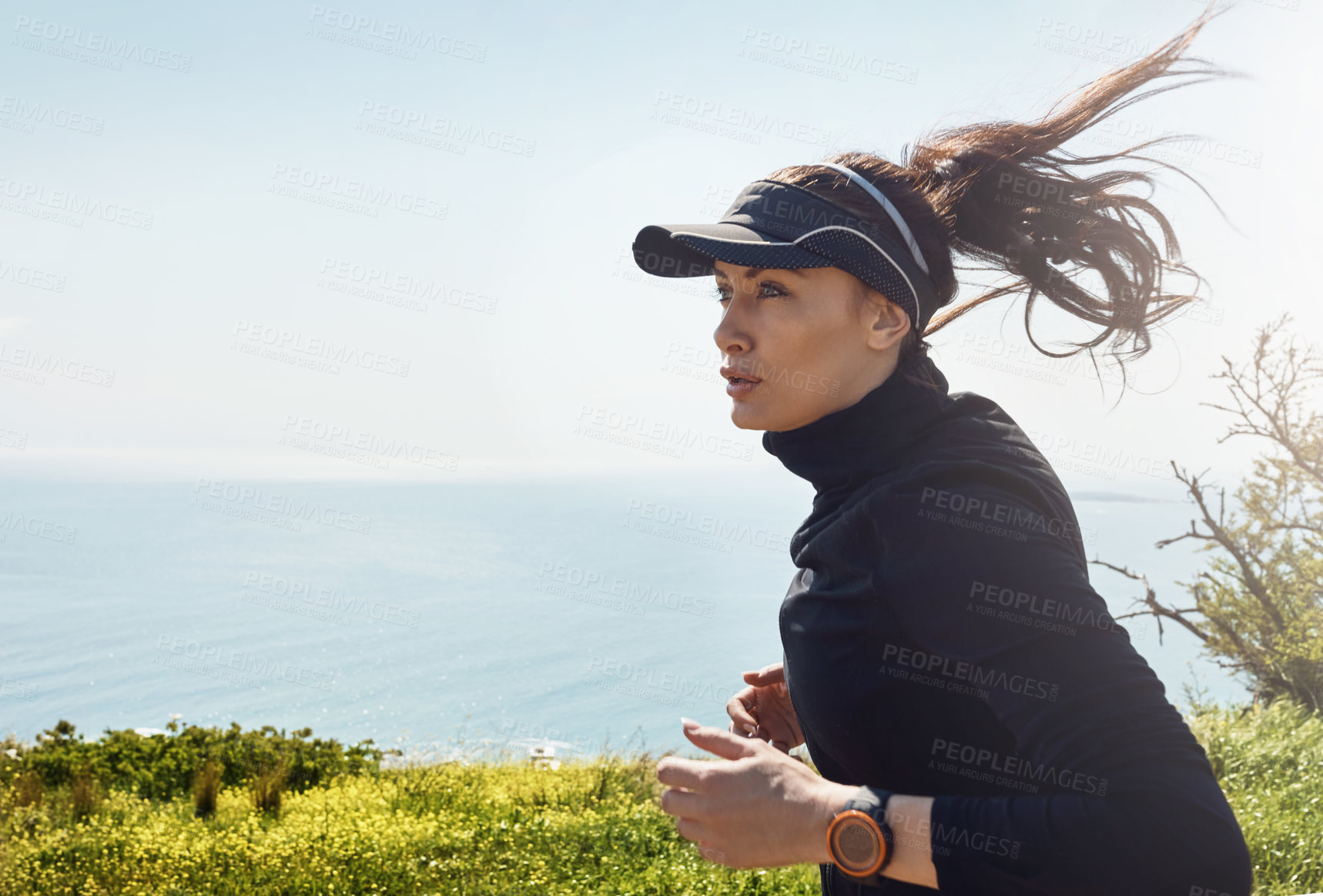 Buy stock photo Shot of a determined young woman going for a jog on her own with a view of the ocean in the background