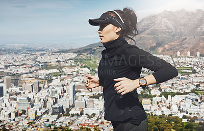 Buy stock photo Shot of a determined young woman going for a jog on her own with a view of the city in the background