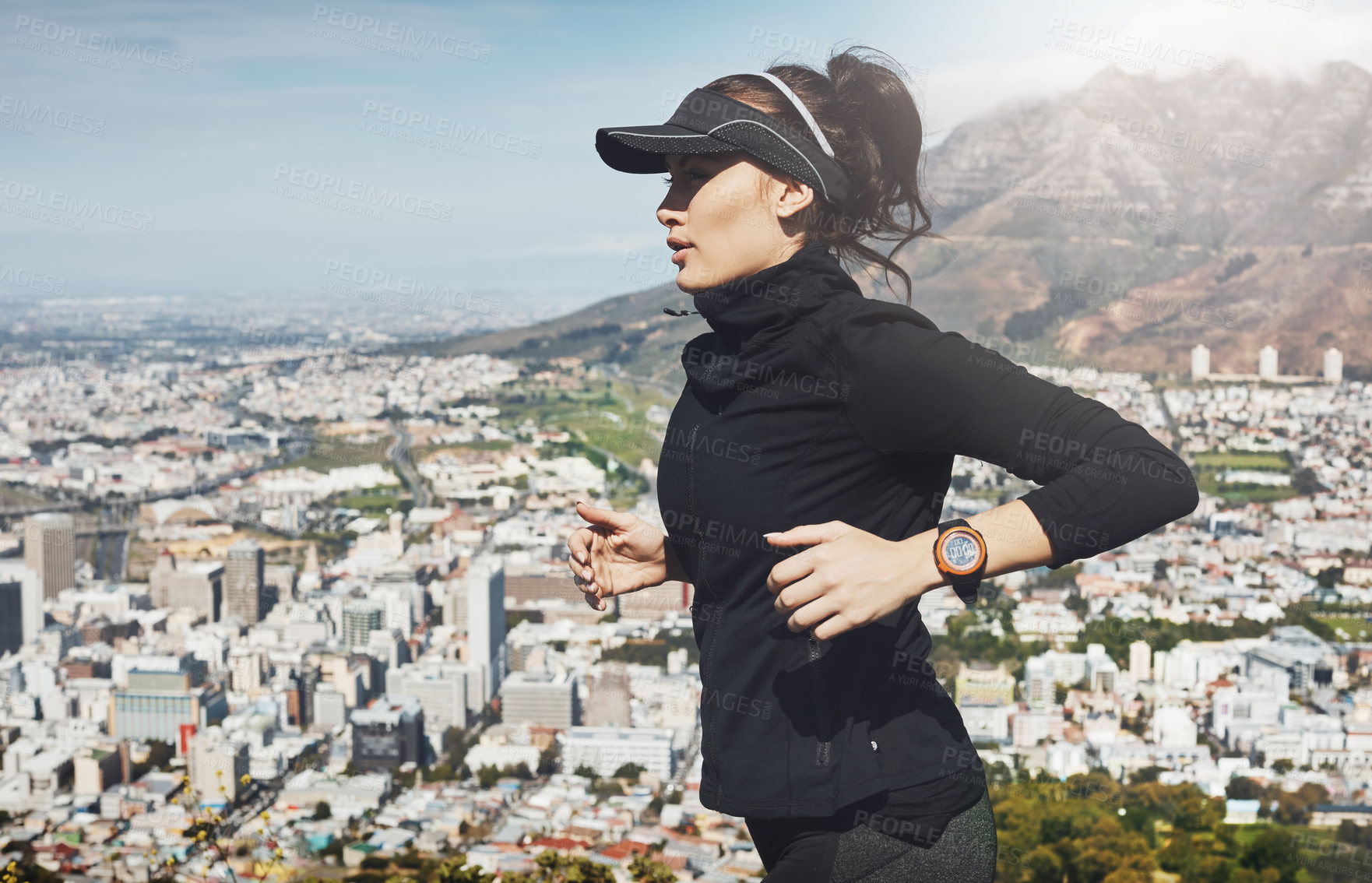 Buy stock photo Shot of a determined young woman going for a jog on her own with a view of the city in the background