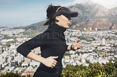 Buy stock photo Shot of a determined young woman going for a jog on her own with a view of the city in the background