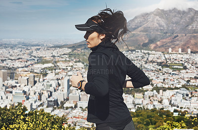Buy stock photo Shot of a determined young woman going for a jog on her own with a view of the city in the background