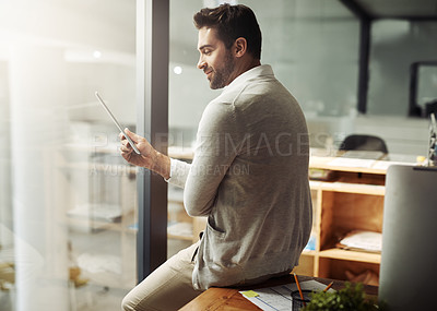 Buy stock photo Shot of a handsome young businessman using a digital tablet while working late in an office
