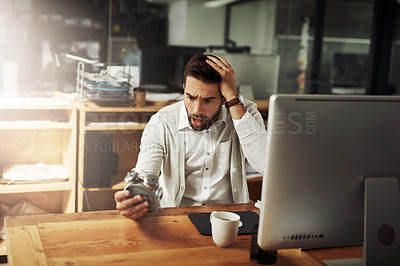 Buy stock photo Shot of a handsome young businessman holding an alarm clock and looking stressed out while working late in an office