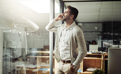 Buy stock photo Shot of a handsome young businessman talking on a cellphone while working late in an office