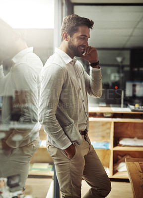 Buy stock photo Shot of a handsome young businessman talking on a cellphone while working late in an office